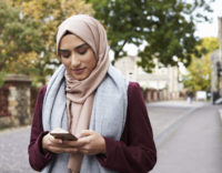 British Muslim Woman Using Mobile Phone In Urban Setting